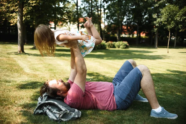 夏の公園で緑の草の上で遊んでいる間楽しみを持つ小さな娘を持つ父 — ストック写真
