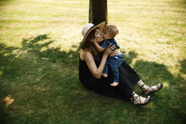 夏の公園で緑の草の上に横たわっている間 幸せな母親は小さな息子と一緒にプライ — ストック写真