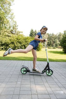 güneşli yaz parkında scooter sürme mavi giysiler içinde sevimli kız 