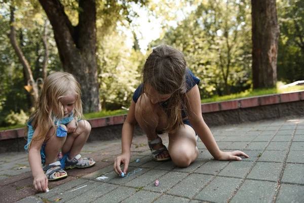 little sisters playing while drawing with crayons on tile road in park