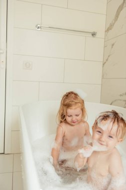 Küçük kardeşi ve kız kardeşi birlikte eğlenceli ve çekici banyo ışık banyoya sahip  
