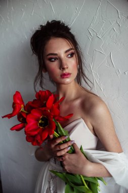 kırmızı lale buketi tutan ve beyaz duvar yakınında poz gelinlik güzel gelin