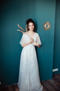 altın dekoratif tüyler tutan ve yeşil duvara yaslanmış güzel gelin 