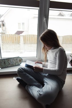 pencerenin yanında oturan ve kitap okuyan kız