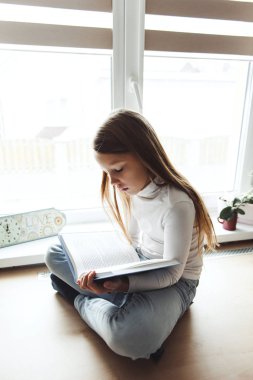 pencerenin yanında oturan ve kitap okuyan kız