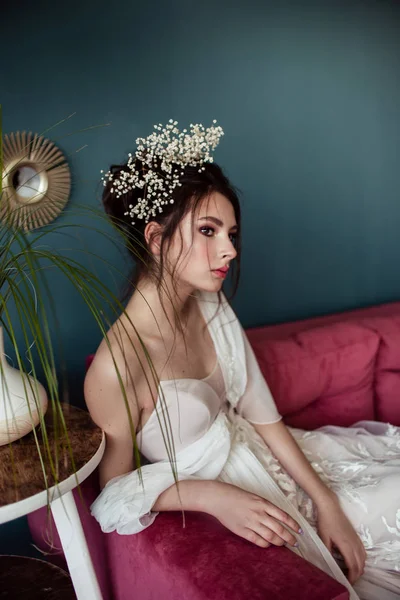 beautiful bride with stylish hairdo in wedding dress sitting on pink sofa