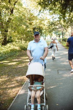 Büyükbaba bir bebek arabasında torununa biniyor.