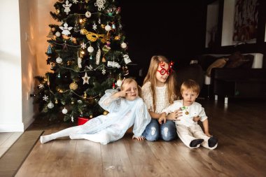 Çocuklar Noel ağacının yanında ışıklarla oynuyorlar.