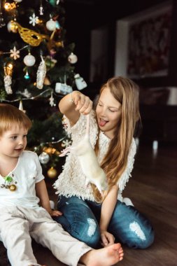 Çocuklar Noel ağacının yanında fareyle oynuyorlar.