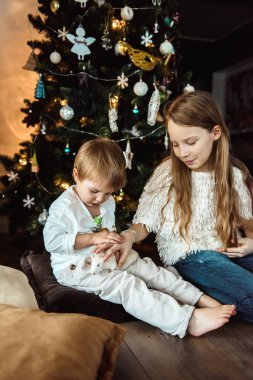 Çocuklar Noel ağacının yanında fareyle oynuyorlar.