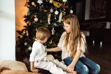 Çocuklar Noel ağacının yanında fareyle oynuyorlar.