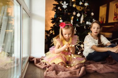 Çocuklar Noel ağacının yanında ışıklarla oynuyorlar.