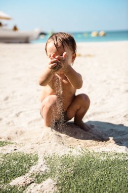 Küçük çocuk kumsalda kumla oynuyor.