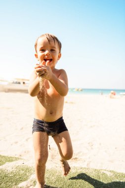 Küçük çocuk kumsalda kumla oynuyor.