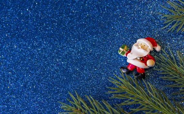 Tatil, kış ve kutlama kavramı. Noel Baba hediye bir parlak mavi arka plan ve köknar dallarda taşıyan ile Noel ve yeni yıl kartı.