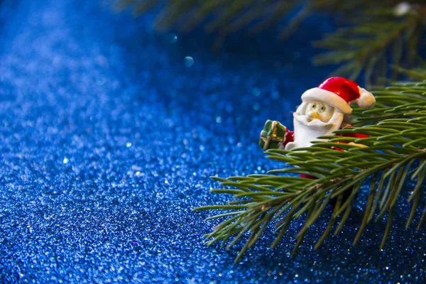 Tatil, kış ve kutlama kavramı. Noel Baba hediye bir parlak mavi arka plan ve köknar dallarda taşıyan ile Noel ve yeni yıl kartı.