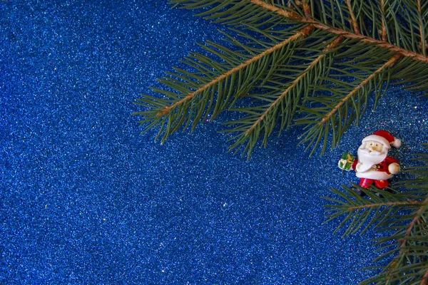 Tatil, kış ve kutlama kavramı. Noel Baba hediye bir parlak mavi arka plan ve köknar dallarda taşıyan ile Noel ve yeni yıl kartı.