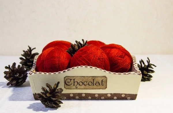 Örgü sepeti ve çam kozalakları beyaz zemin üzerine kırmızı iplik. Yün topları sepetle. Kırmızı örgü yün.