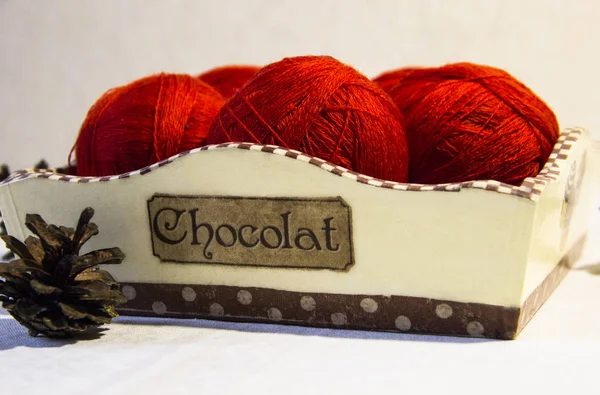 Örgü sepeti ve çam kozalakları beyaz zemin üzerine kırmızı iplik. Yün topları sepetle. Kırmızı örgü yün.