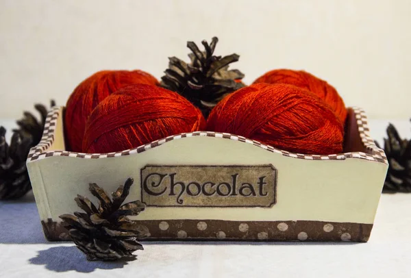 Örgü sepeti ve çam kozalakları beyaz zemin üzerine kırmızı iplik. Yün topları sepetle. Kırmızı örgü yün.