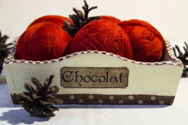 Örgü sepeti ve çam kozalakları beyaz zemin üzerine kırmızı iplik. Yün topları sepetle. Kırmızı örgü yün.