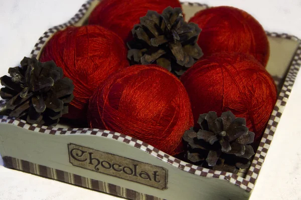 Örgü sepeti ve çam kozalakları beyaz zemin üzerine kırmızı iplik. Yün topları sepetle. Kırmızı örgü yün.