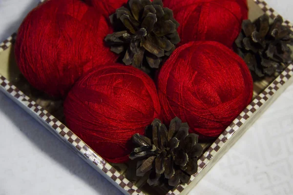 Örgü sepeti ve çam kozalakları beyaz zemin üzerine kırmızı iplik. Yün topları sepetle. Kırmızı örgü yün.