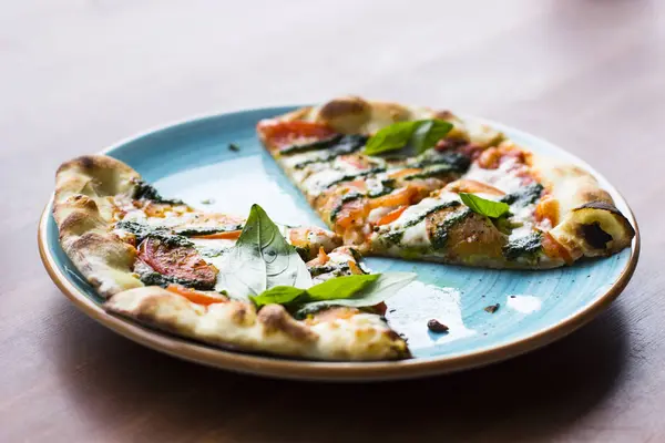 Pizza Margarita veya Margherita yalan bir ahşap masa arka plan mavi bir tabağa dilimlenmiş, görünümü top. Pizza domates, taze fesleğen, Mozzarella peyniri, biber ve baharat ile kapatın. Geleneksel İtalyan yemekleri.