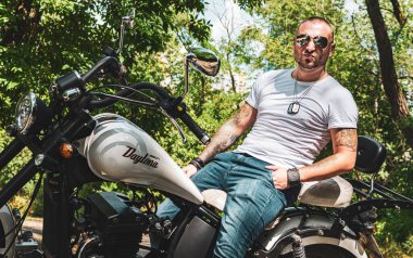 Kyiv 'deki Geon Daytona motosikletinde dövmeli, sakallı ve bilezikli genç yakışıklı bir adam.