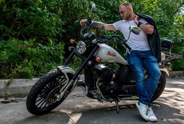 Kyiv 'deki Geon Daytona motosikletinde dövmeli, sakallı ve bilezikli genç yakışıklı bir adam.