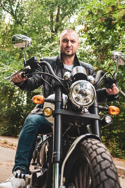 Young handsome man with tattoos and beard and bracelets on Geon Daytona motorcycle in Kyiv