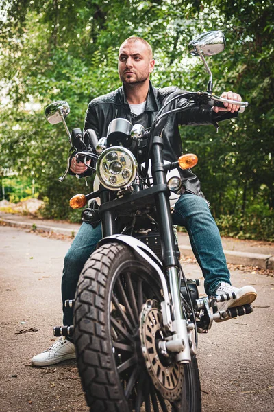 Kyiv 'deki Geon Daytona motosikletinde dövmeli, sakallı ve bilezikli genç yakışıklı bir adam.