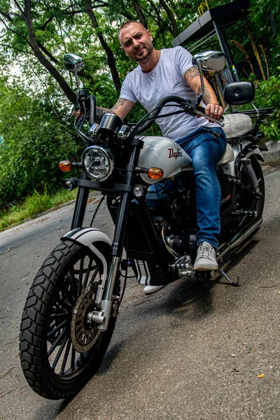 Kyiv 'deki Geon Daytona motosikletinde dövmeli, sakallı ve bilezikli genç yakışıklı bir adam.