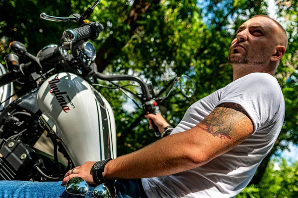 Kyiv 'deki Geon Daytona motosikletinde dövmeli, sakallı ve bilezikli genç yakışıklı bir adam.