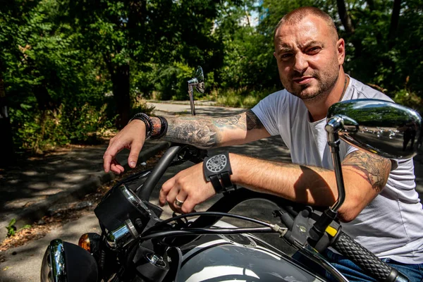 Kyiv 'deki Geon Daytona motosikletinde dövmeli, sakallı ve bilezikli genç yakışıklı bir adam.