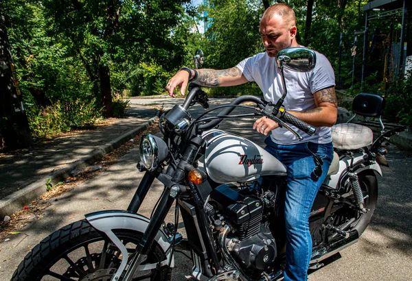 Kyiv 'deki Geon Daytona motosikletinde dövmeli, sakallı ve bilezikli genç yakışıklı bir adam.