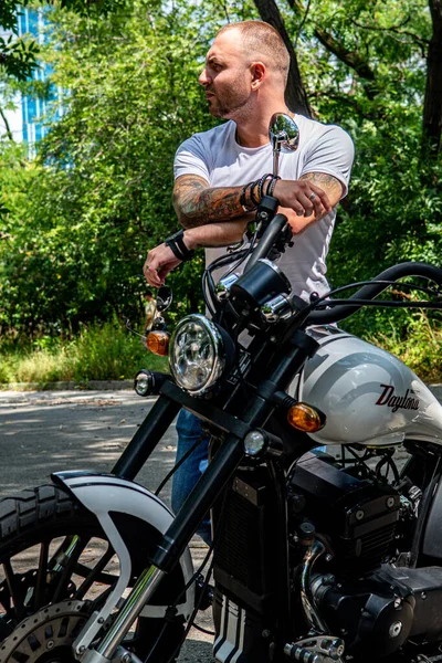 Kyiv 'deki Geon Daytona motosikletinde dövmeli, sakallı ve bilezikli genç yakışıklı bir adam.