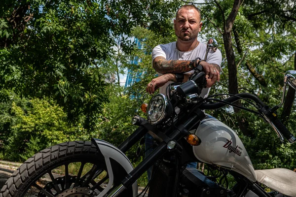 Kyiv 'deki Geon Daytona motosikletinde dövmeli, sakallı ve bilezikli genç yakışıklı bir adam.
