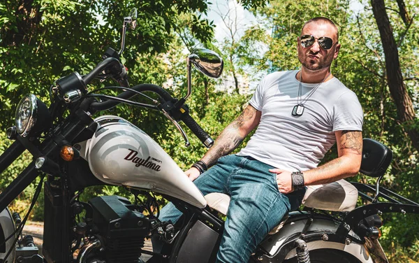 Kyiv 'deki Geon Daytona motosikletinde dövmeli, sakallı ve bilezikli genç yakışıklı bir adam.