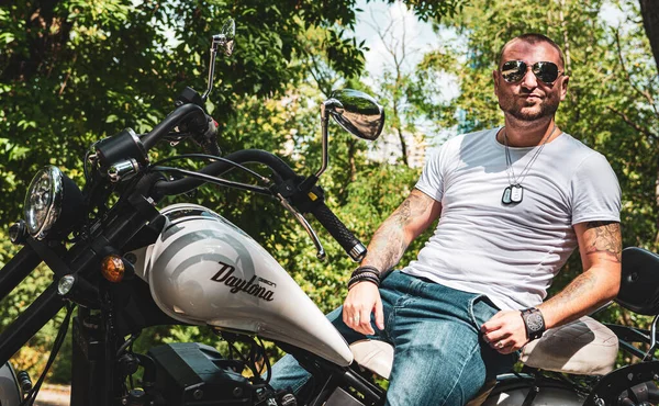 Kyiv 'deki Geon Daytona motosikletinde dövmeli, sakallı ve bilezikli genç yakışıklı bir adam.