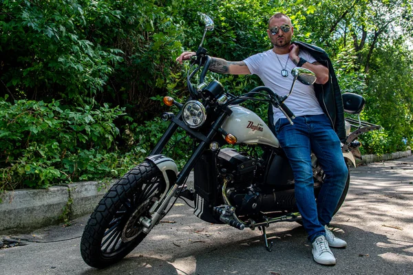 Kyiv 'deki Geon Daytona motosikletinde dövmeli, sakallı ve bilezikli genç yakışıklı bir adam.