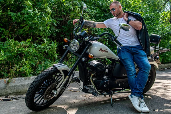 Kyiv 'deki Geon Daytona motosikletinde dövmeli, sakallı ve bilezikli genç yakışıklı bir adam.