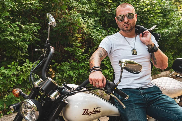 Kyiv 'deki Geon Daytona motosikletinde dövmeli, sakallı ve bilezikli genç yakışıklı bir adam.