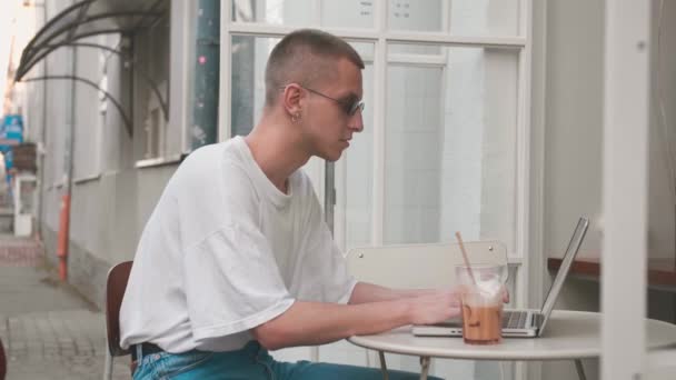 Jóképű kaukázusi homoszexuális szabadúszó üzletember szorgalmasan dolgozik a laptopon a kávézóban. Férfi gépel a billentyűzeten, és keres új munkát az interneten a coffeeshop. Üzleti koncepció — Stock videók