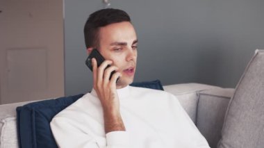 Genç beyaz adam telefon kullanıyor. Evdeki koltukta rahatla.