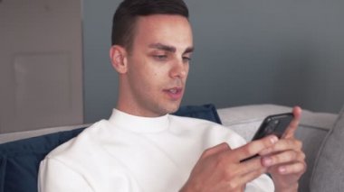 Genç beyaz adam telefon kullanıyor. Evdeki koltukta rahatla.