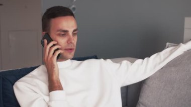 Genç beyaz adam telefon kullanıyor. Evdeki koltukta rahatla.