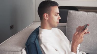 Genç beyaz adam telefon kullanıyor. Evdeki koltukta rahatla.