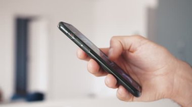 Bir evde ya da ofiste akıllı telefon kullanan genç bir adamın yavaş çekimde ellerini kapat.