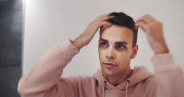 Genç beyaz adam tuvalette aynaya bakıyor, saçını düzeltiyor, sabahları yakışıklı genç adam.